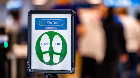 Letrero de TSA PreCheck con huellas indica “ID sin contacto” y “Párese aquí” en un control de seguridad.