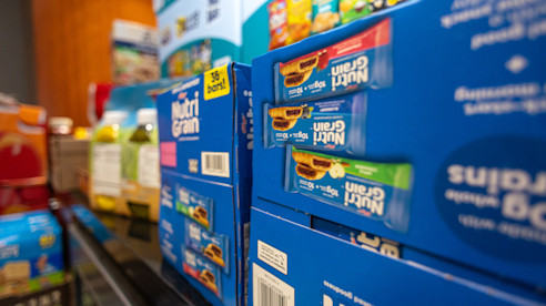Boxes of Nutri-Grain bars stacked on a  shelf with other snack items in the background.