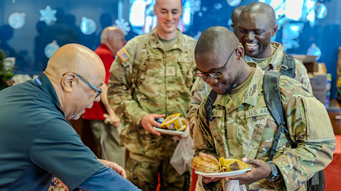 Miembros del ejército de EE. UU. sonríen mientras reciben comida de un voluntario durante un evento festivo en el aeropuerto.