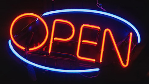 Un letrero de neón brillante muestra la palabra “OPEN” en rojo rodeada por un borde ovalado azul.