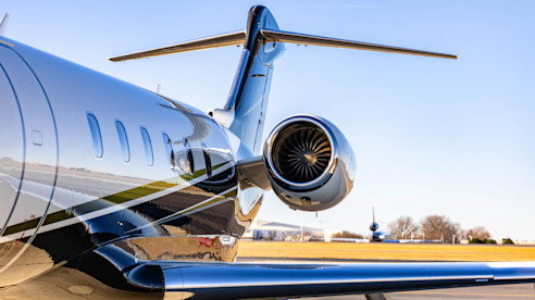 Close-up of a private jet's engine and tail on a sunny day at an airport runway.
